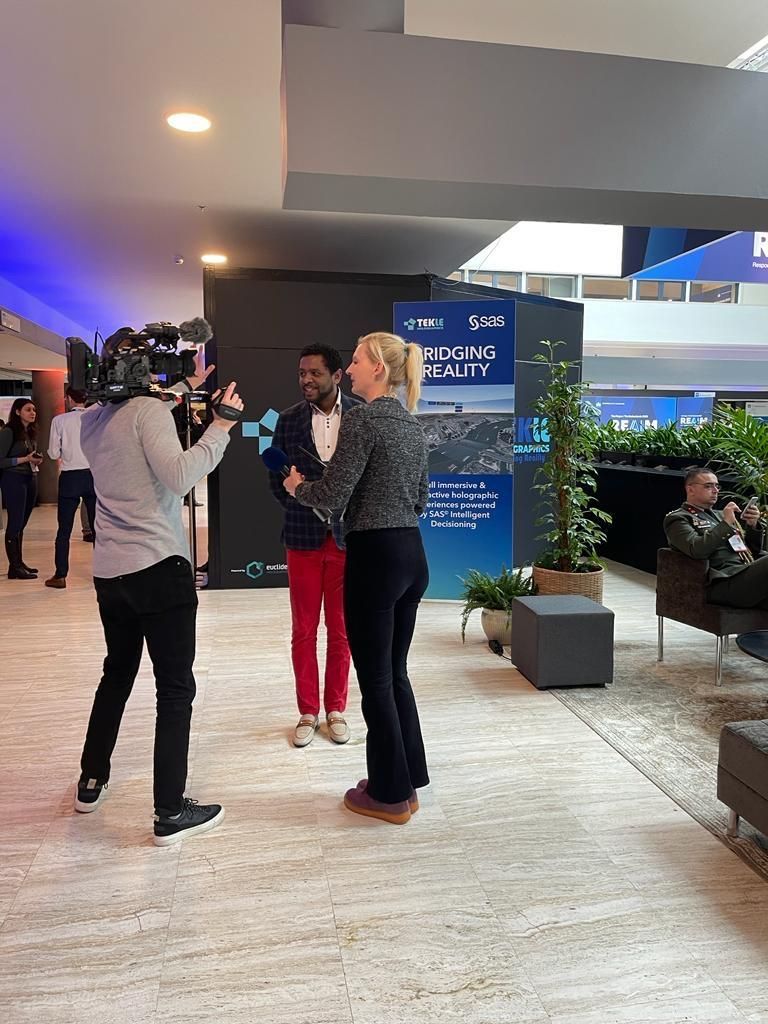 Michel Tzsfaldet wird beim REAIM-2023-Gipfel vor der Kamera interviewt, vor einem Banner von Tekle Holographics und SAS.